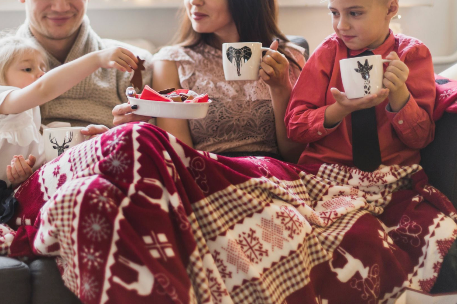 Familia celebrando la Navidad juntos con bebidas calientes y galletas bajo una manta festiva