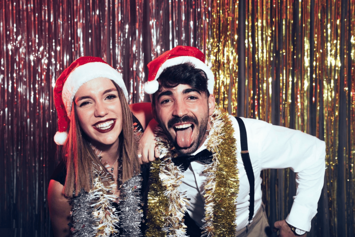 Amigos celebrando una fiesta de Navidad con gorros de Papá Noel y guirnaldas brillantes