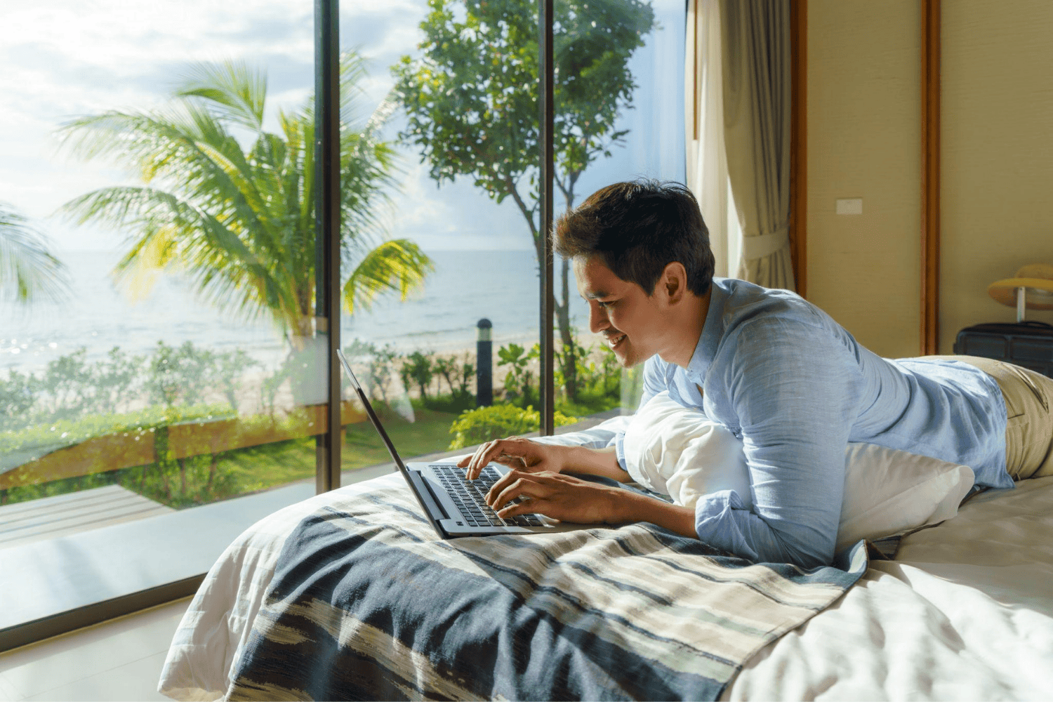Persona trabajando en su laptop dentro de un apartamento moderno con grandes ventanales y vista al mar.